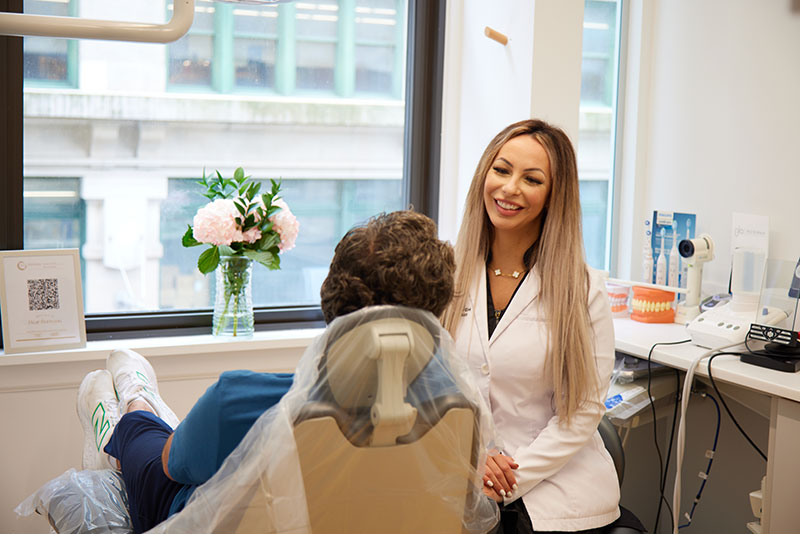 Dentist in white coat consulting with patient in dental chair, bright office setting with flowers and dental tools, emphasizing personalized care in implant dentistry.