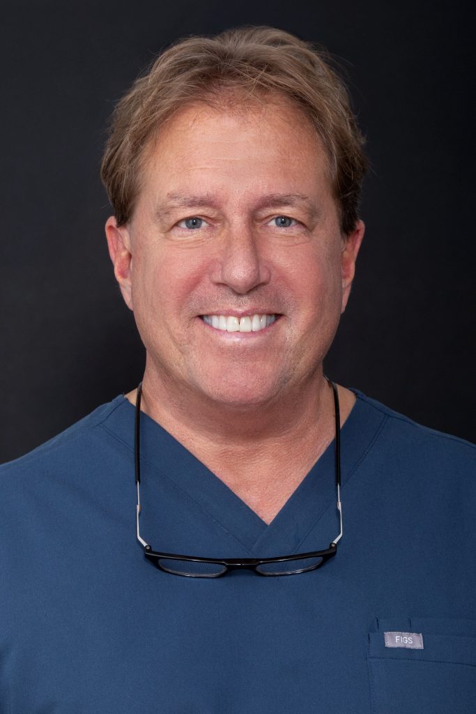 Dr. Robert Castracane, DMD, smiling in dental scrubs, showcasing expertise in implant dentistry at Advanced Implant & Cosmetic Dentistry in New York.