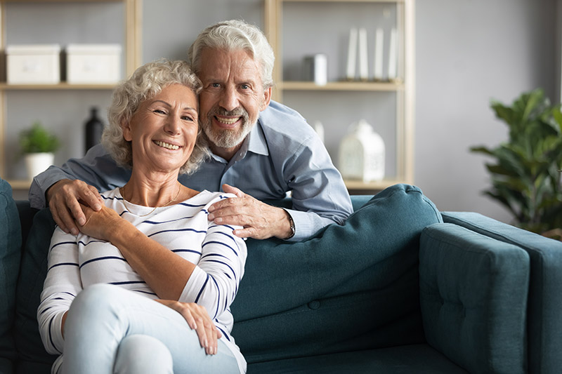 Smiling senior couple sitting on a couch, showcasing a happy relationship, relevant to same-day dental implants and restoring smiles in NYC.